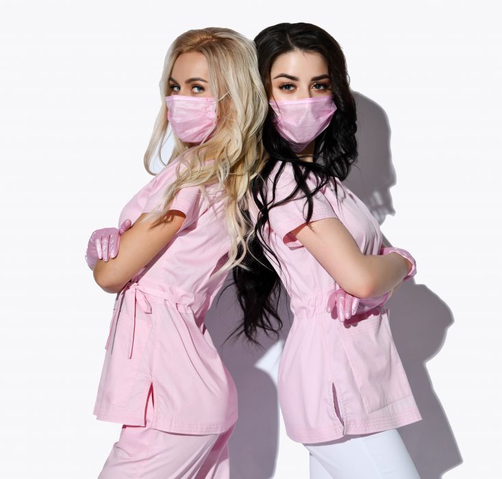 Two ladies in pink uniform, disposable gloves and medical masks are posing